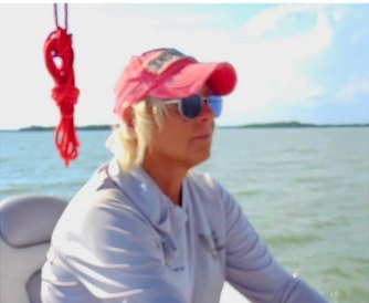 Captain Jamie in a red visor at the helm on open water