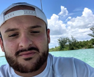 Captain Jonallen Velazquez in a backwards cap with turquoise water and mangroves behind him