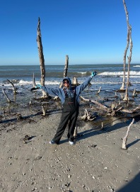 First Mate Veronica with her arms raised on a driftwood-strewn shell beach