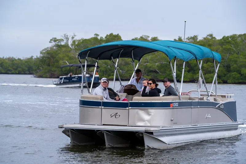 Guests and a captain aboard the teal-canopied Avalon pontoon underway along a mangrove shoreline, with a second Sand Dollar pontoon running behind