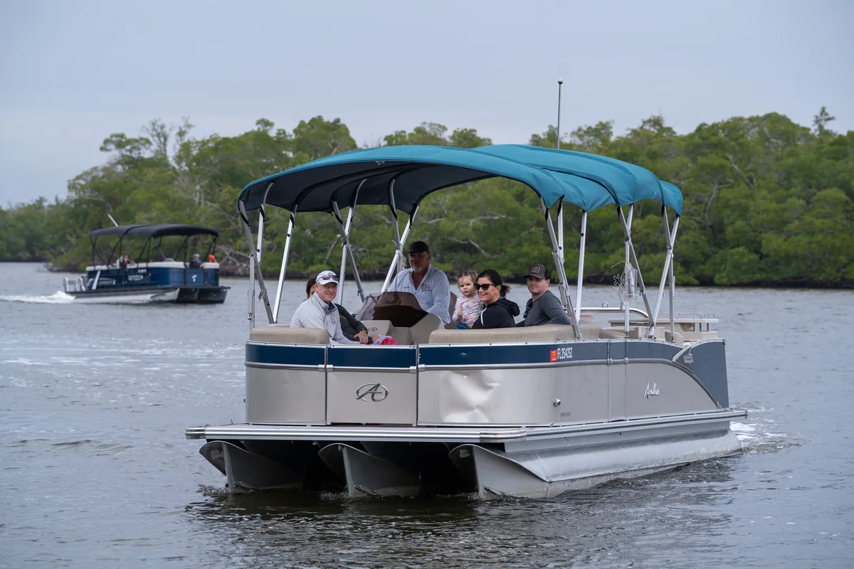 The Avalon pontoon with teal biminis carrying a family with a toddler through a mangrove channel