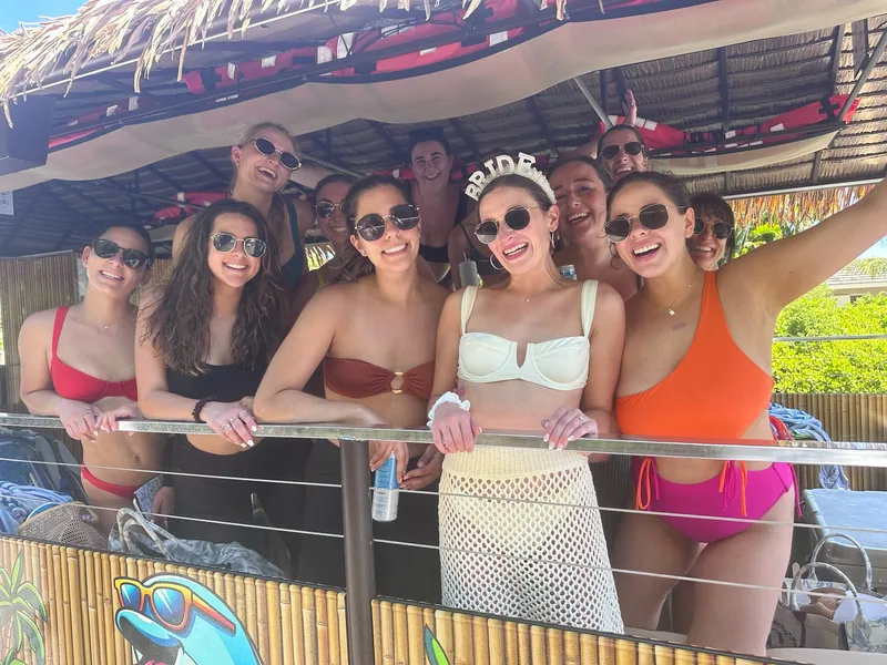 The bride in her pearl crown laughing with her friends along the tiki boat railing