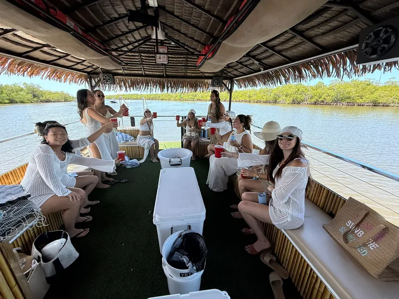 A bachelorette group in white raising a toast from the tiki boat's bench seats in a mangrove channel