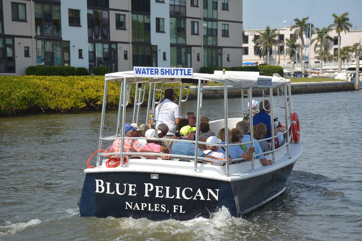 The Blue Pelican water shuttle full of guests on Naples Bay, its navy transom lettered Blue Pelican, Naples FL