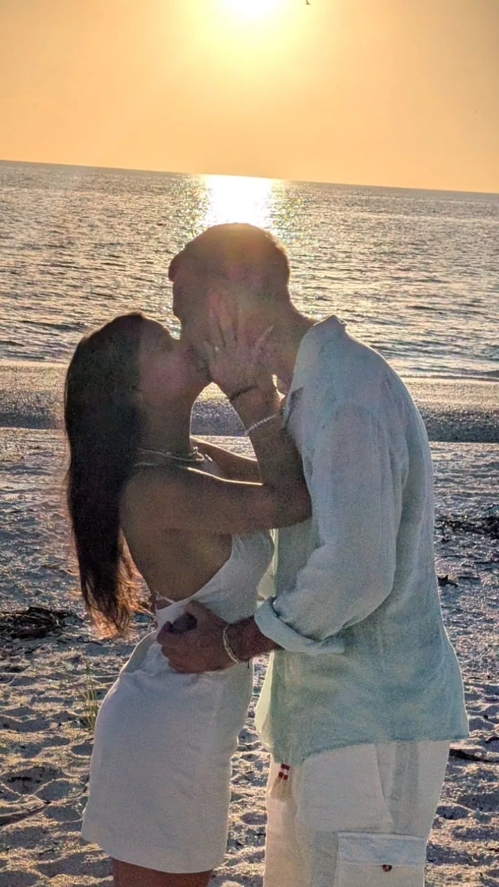 A couple kissing at the shoreline as the sun sets over the Gulf