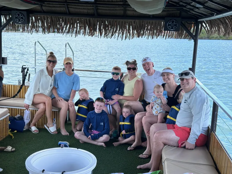 A multigenerational family on the tiki boat's bench seats, the little ones buckled into life jackets