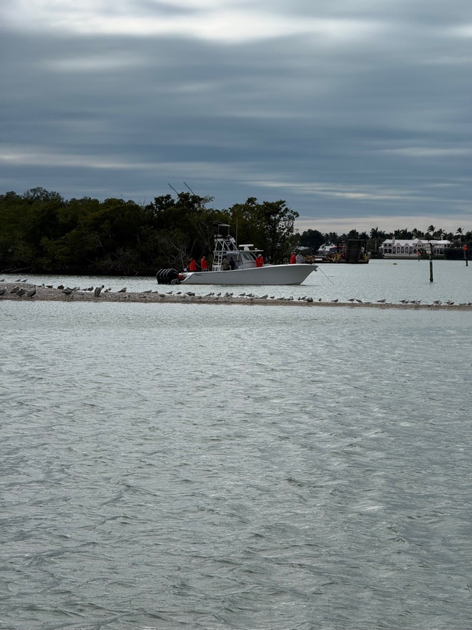 A center-console fishing boat anchored beside a bird-covered sandbar on an overcast day near Marco Island, Florida