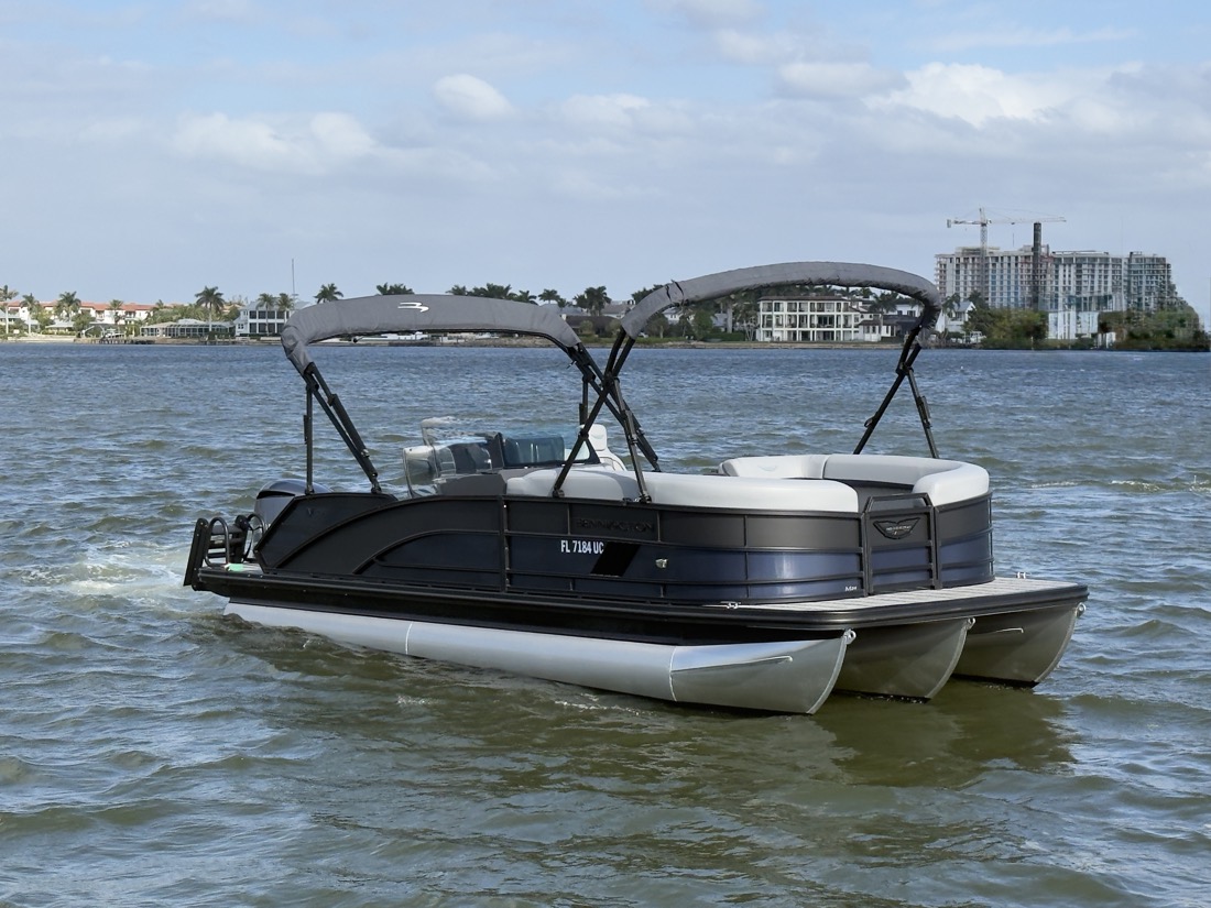 A Sand Dollar Bennington pontoon boat with shade tops on the calm water of Naples Bay with the Naples waterfront behind it