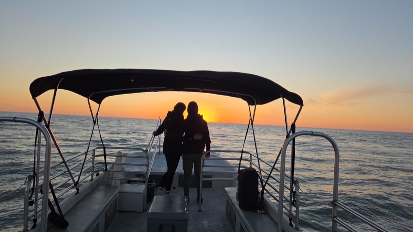 A couple silhouetted on the bow of a boat against a golden Gulf sunset on a Sand Dollar cruise, Marco Island