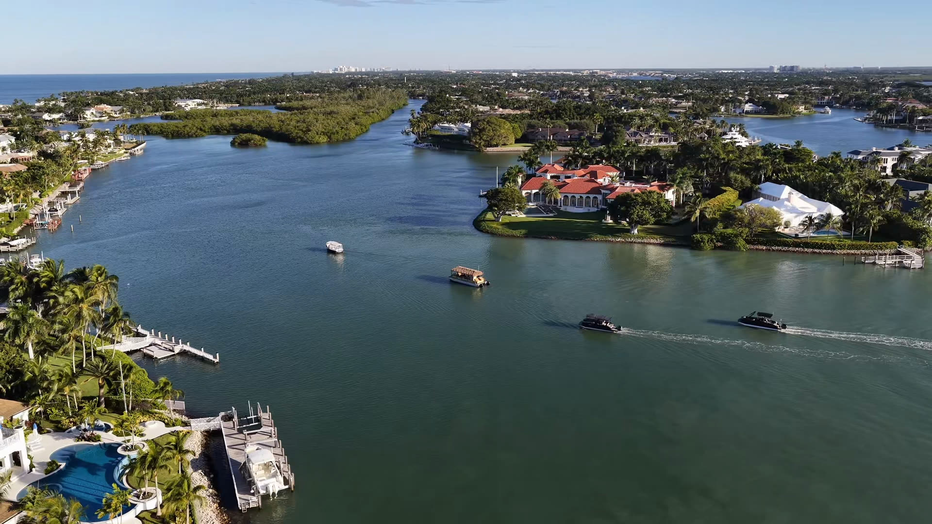 Sand Dollar drone footage: waterfront homes along the bay, the Blue Pelican water shuttle heading out, shelling on a barrier-island beach, and boats running through the mangroves and over the sandbars below the Marco Island skyline