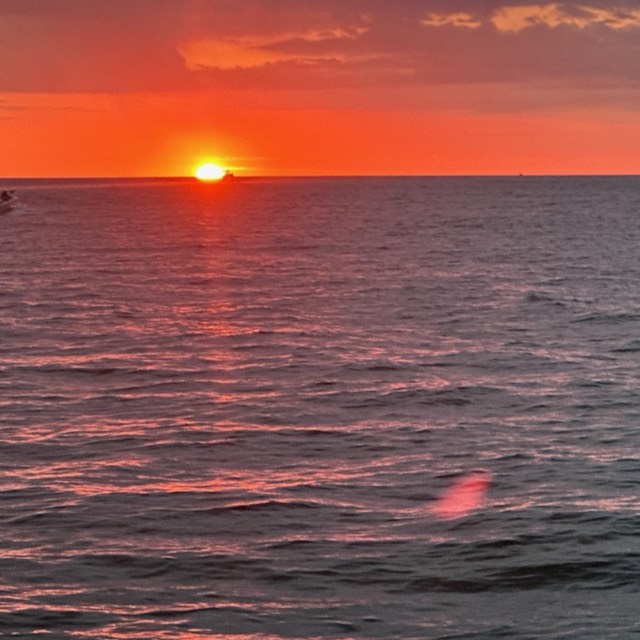 A fiery orange sunset touching the horizon over the Gulf of Mexico, seen from a boat off Naples, Florida