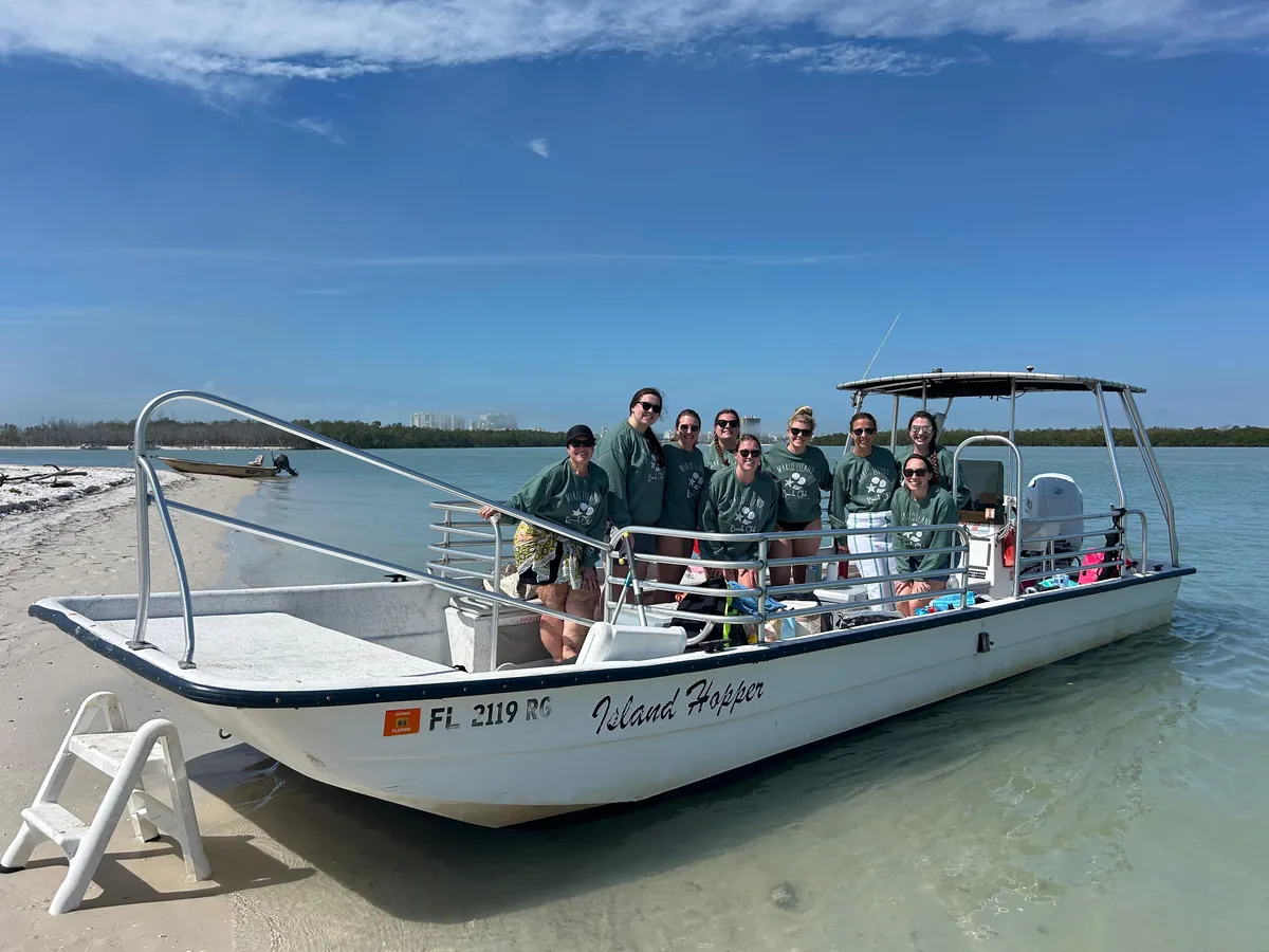 A group of guests in matching green sweatshirts aboard the Island Hopper, beached on a sandy island shore near Marco Island, Florida