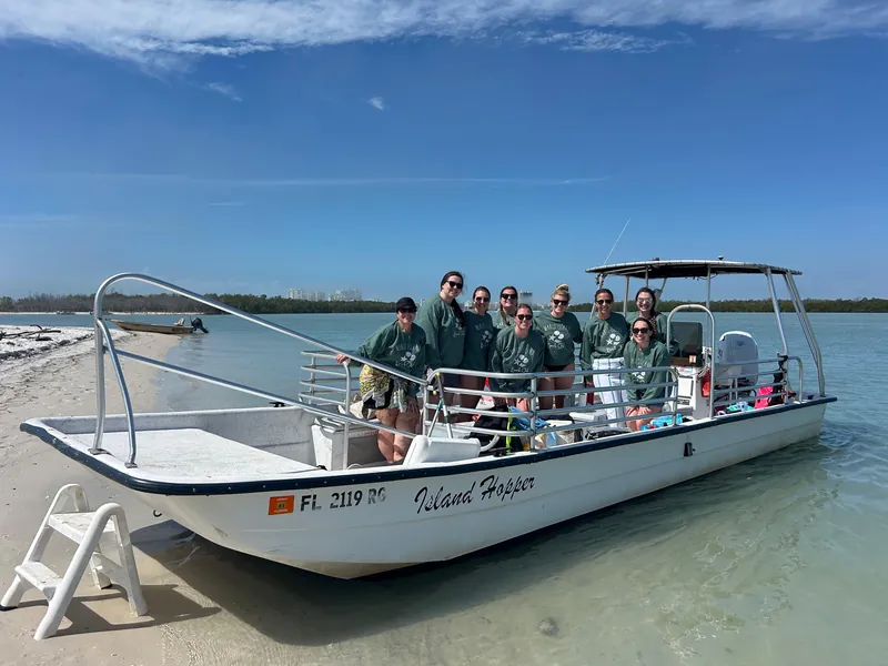 A group of guests in matching green sweatshirts aboard the Island Hopper, beached on a sandy island shore near Marco Island, Florida