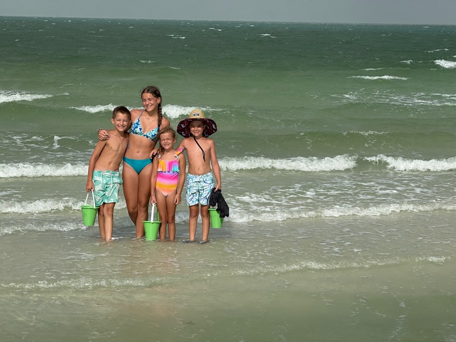 Four children standing in the shallow Gulf surf holding sand buckets on a family shelling trip near Naples, Florida