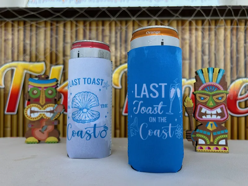 Last Toast on the Coast koozies posed beside carved tiki figures aboard the Tiki Time boat
