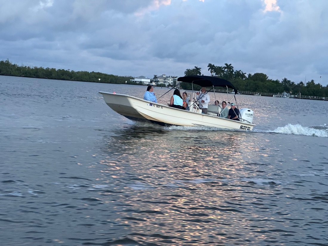 A Sand Dollar charter boat with a few guests aboard cruising calm water past waterfront homes near Naples, Florida, at dusk