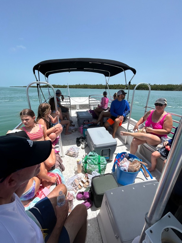 Guests relaxing in the shade aboard a Sand Dollar boat with a mangrove island behind them near Naples, Florida