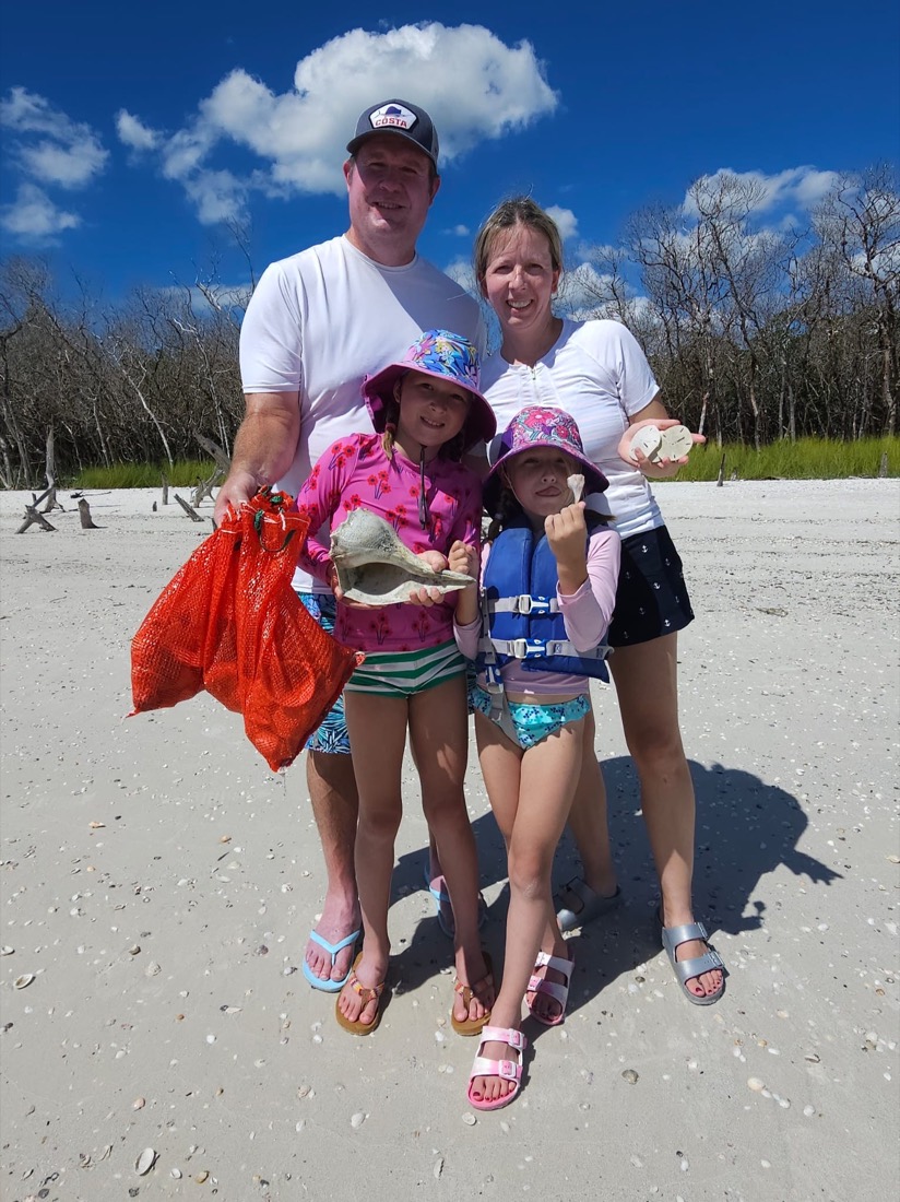 A happy family holding a bag of shells they collected on a Sand Dollar shelling tour, white-sand beach near Marco Island, Florida