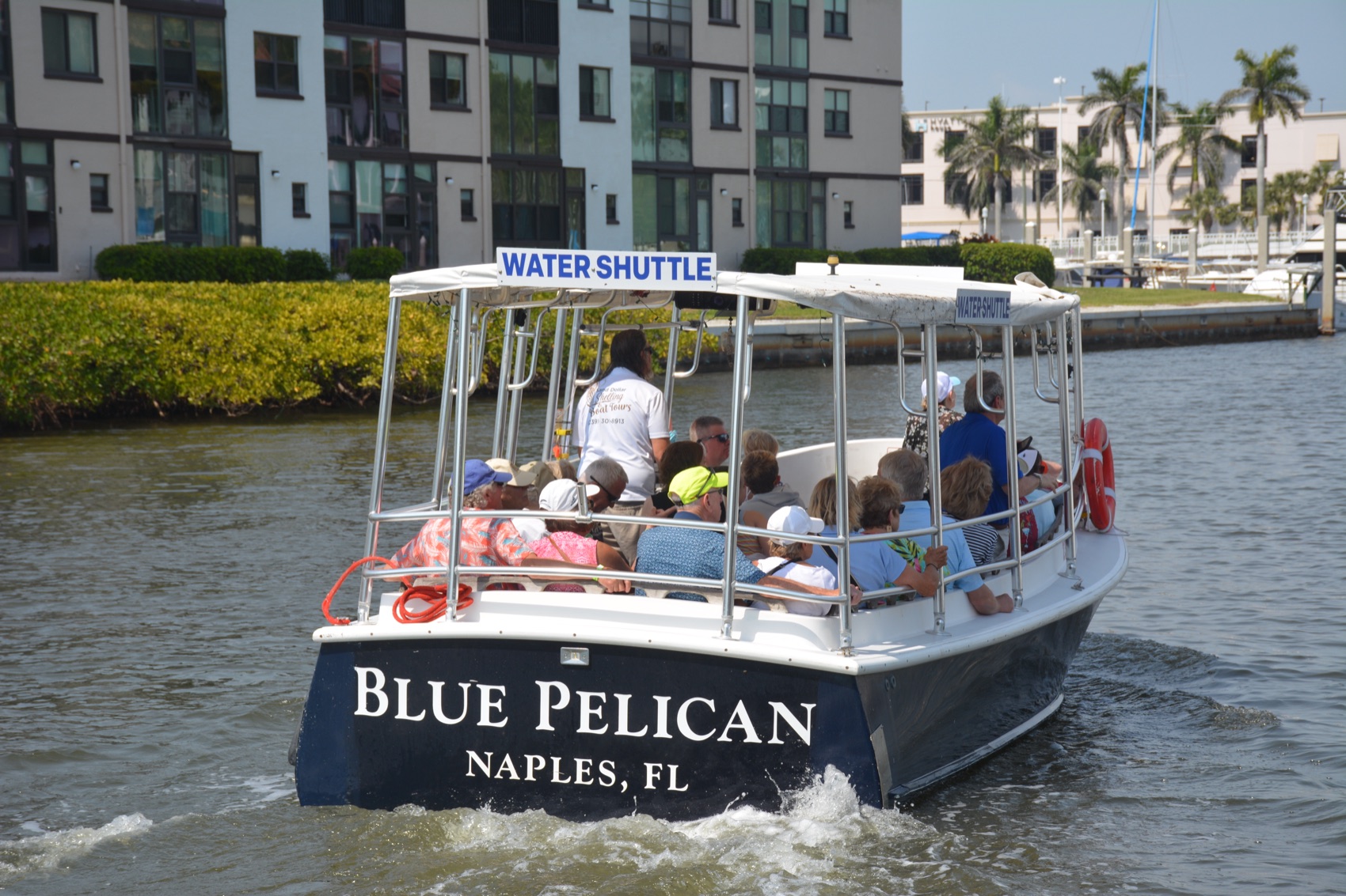 Our Blue Pelican water shuttle carrying guests along Naples Bay past waterfront buildings in Naples, Florida