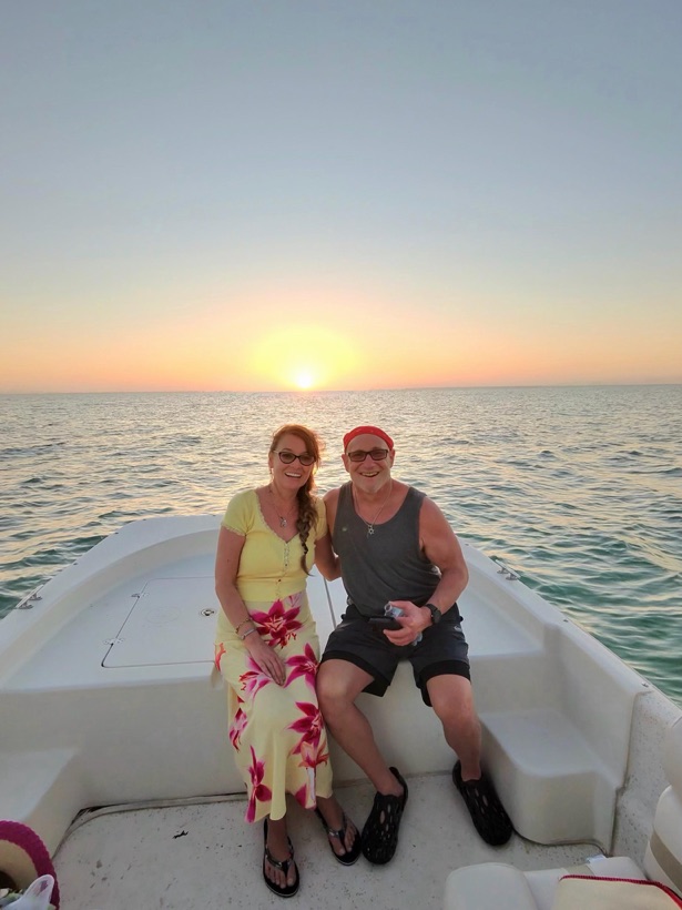 A couple sitting on the bow of a Sand Dollar boat as the sun sets over the Gulf near Naples, Florida