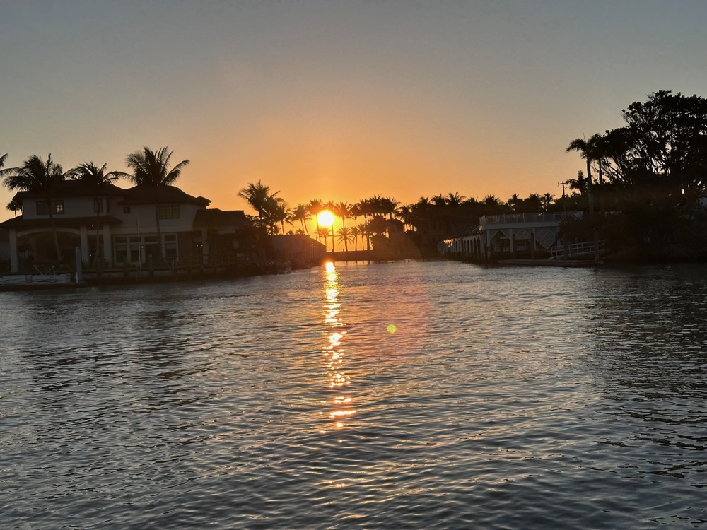 The sun dropping between palms and waterfront homes along a Naples, Florida waterway, seen from the water