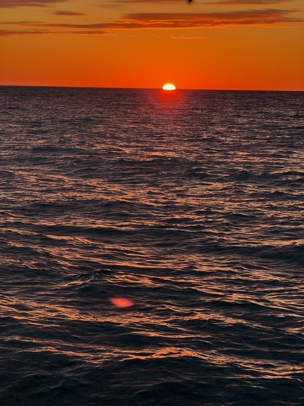 A deep orange sun sitting on the Gulf of Mexico horizon, seen from the water off Naples, Florida