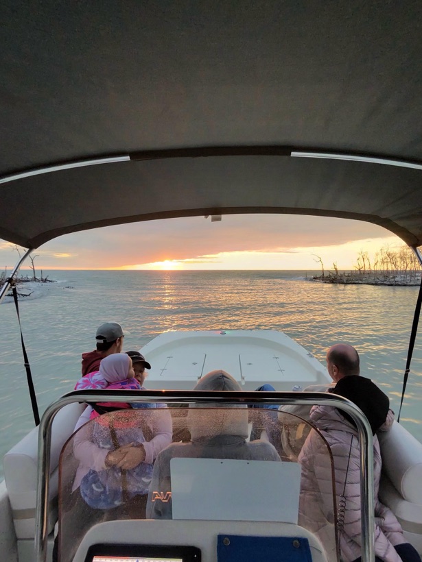 A family watching the sun set over the water from the shaded deck of a Sand Dollar boat near Naples, Florida