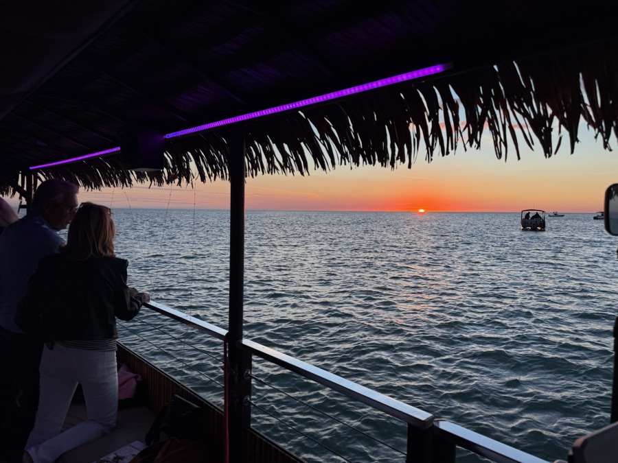 Guests at the rail of a thatched-roof Sand Dollar boat watching the sun drop into the Gulf near Naples, Florida
